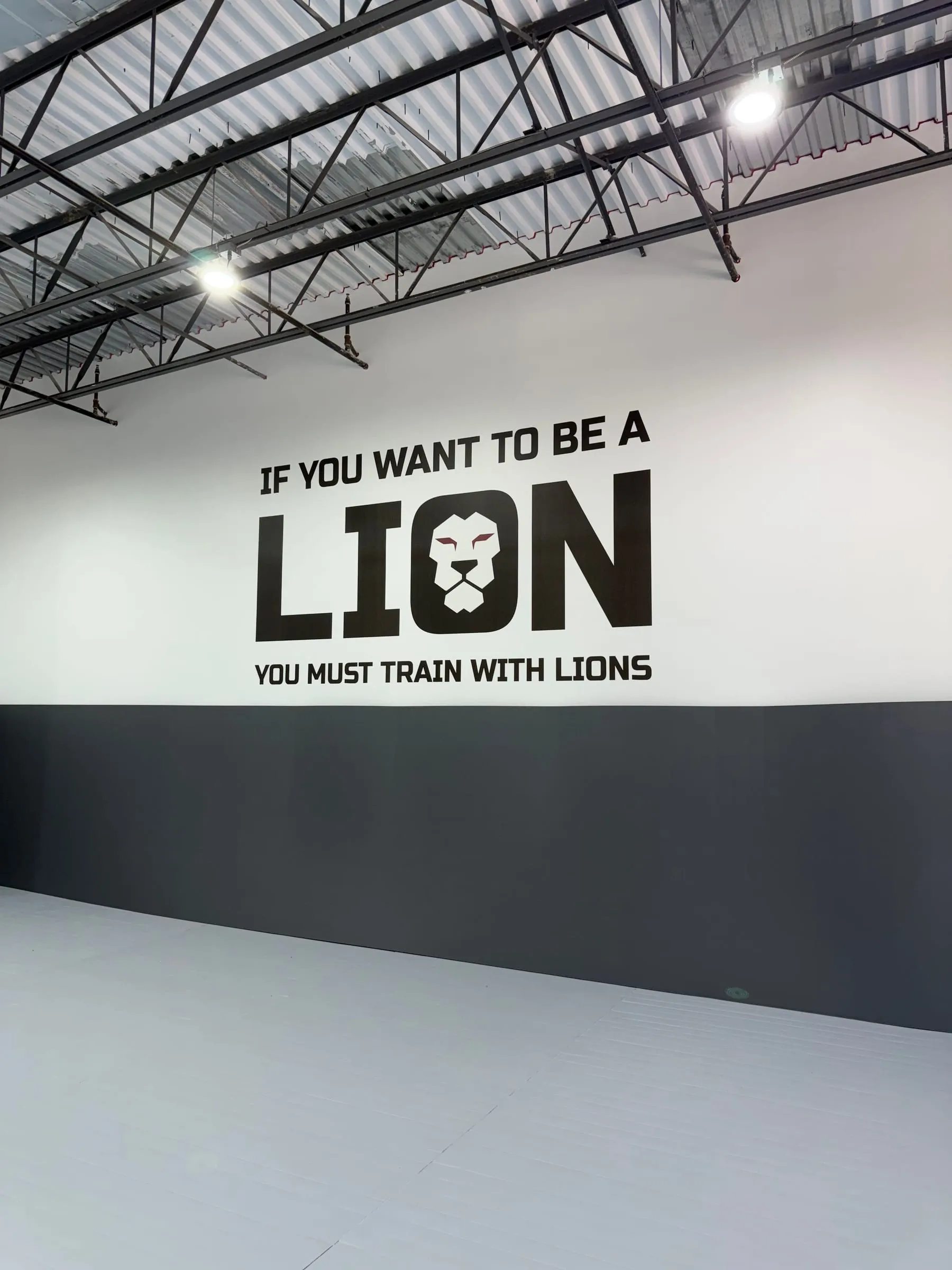 “If you want to be a lion, you must train with lions” in bold black type with a lion logo, printed on a white gym wall