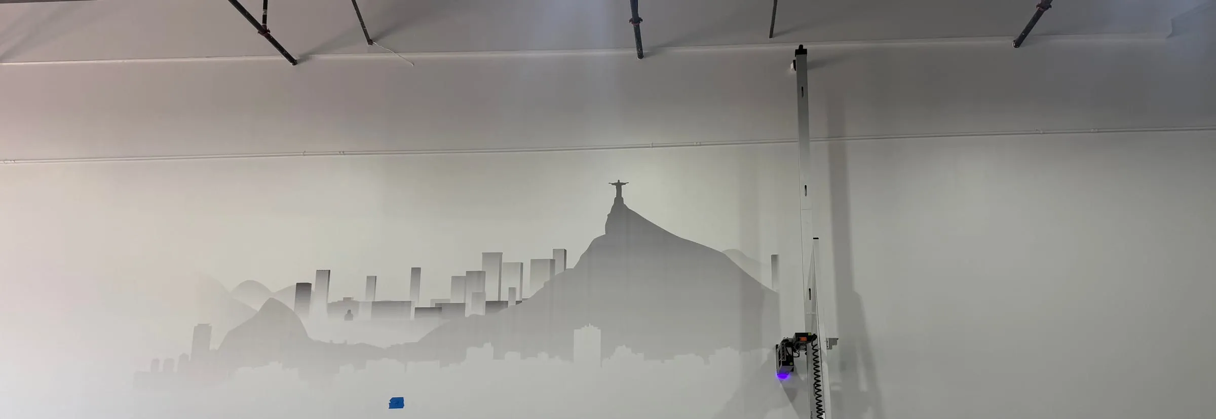 Vertical wall printer on its rail beside a half-printed grey Rio de Janeiro skyline